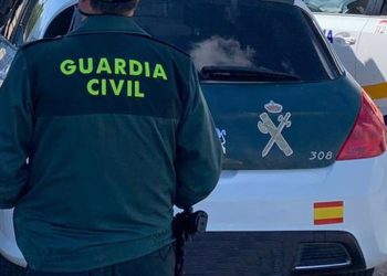 Un agente de la Guardia Civil de espaldas y junto a un vehículo oficial del cuerpo