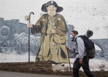 Imagen de archivo de un peregrino pasando ante el mural de Zapatones, en Portomarín, mientras recorre el Camino Francés | EUROPA PRESS