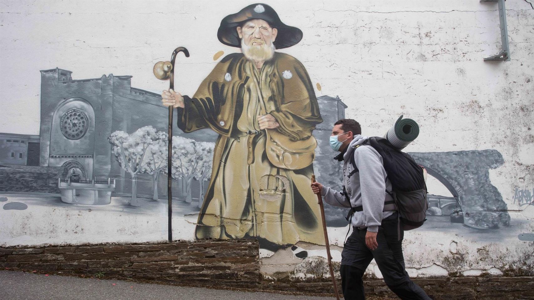Imagen de archivo de un peregrino pasando ante el mural de Zapatones, en Portomarín, mientras recorre el Camino Francés | EUROPA PRESS