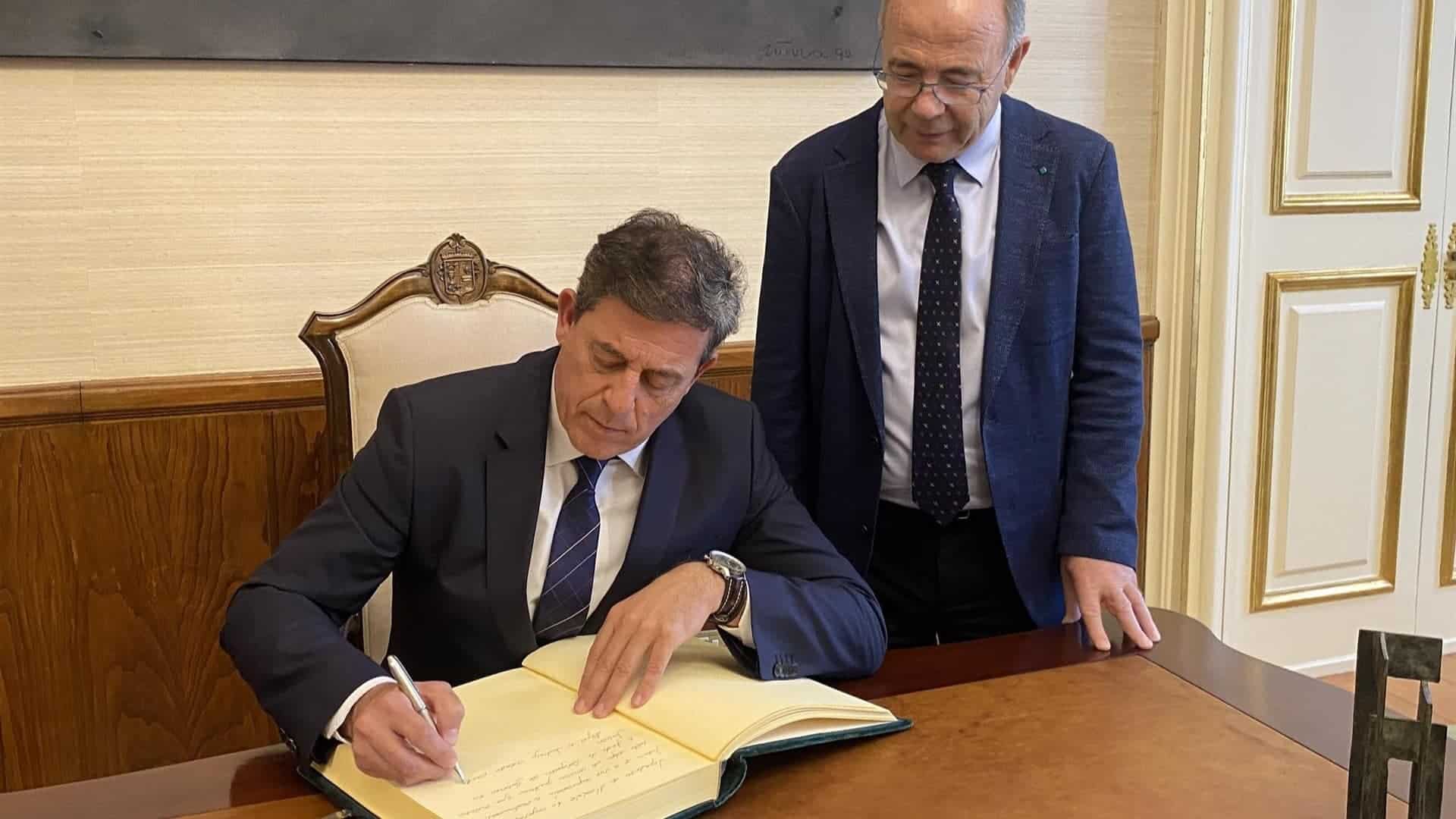 El delegado del Gobierno en Galicia, José Ramón Gómez Besteiro, firma en el libro oficial del Concello de Santiago acompañado por el alcalde, Xosé Sánchez Bugallo | DELEGACIÓN DEL GOBIERNO