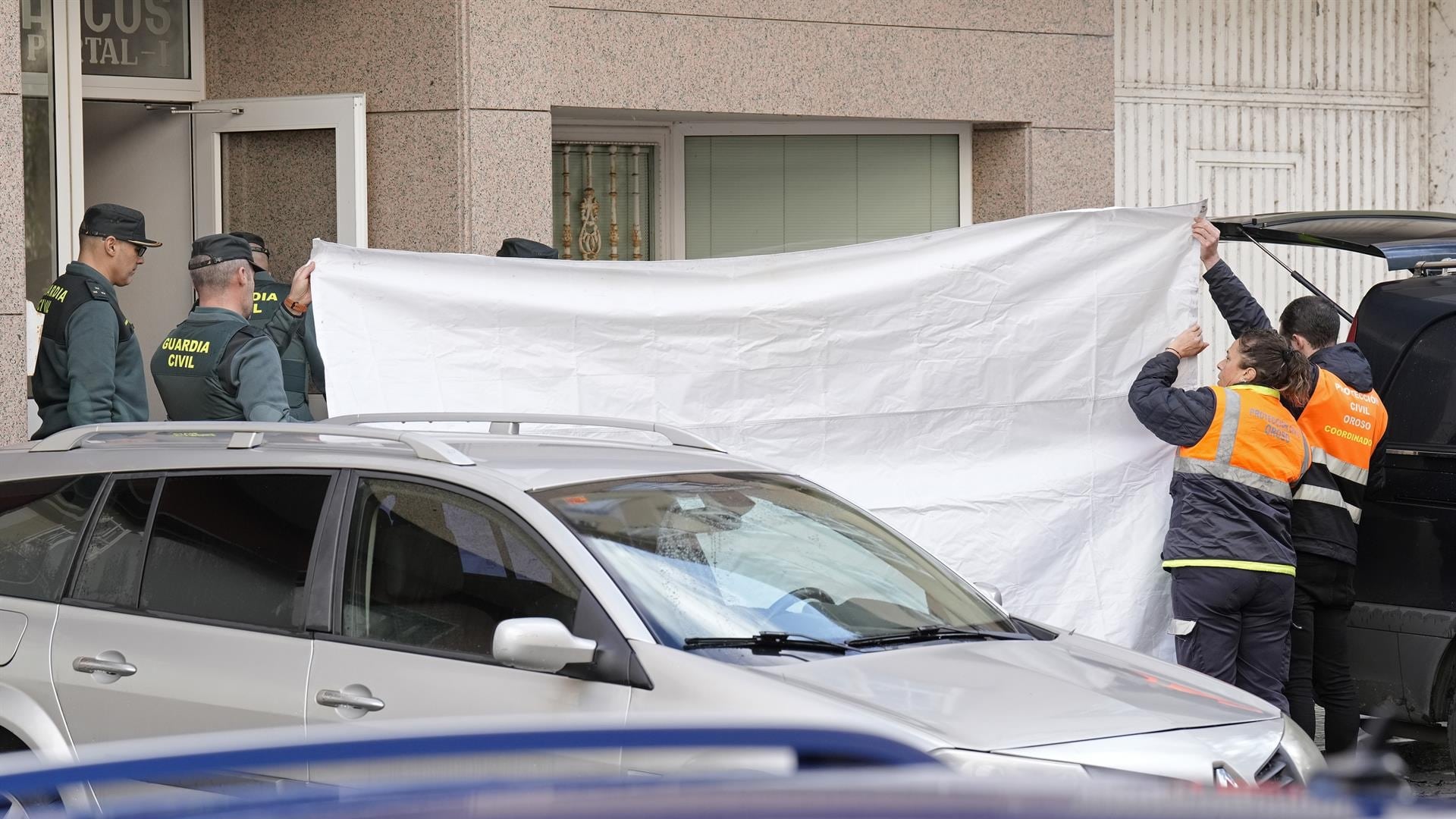 Dos agentes de Protección Civil tapan con una lona la entrada de la vivienda donde se han encontrado los cuerpos | EP