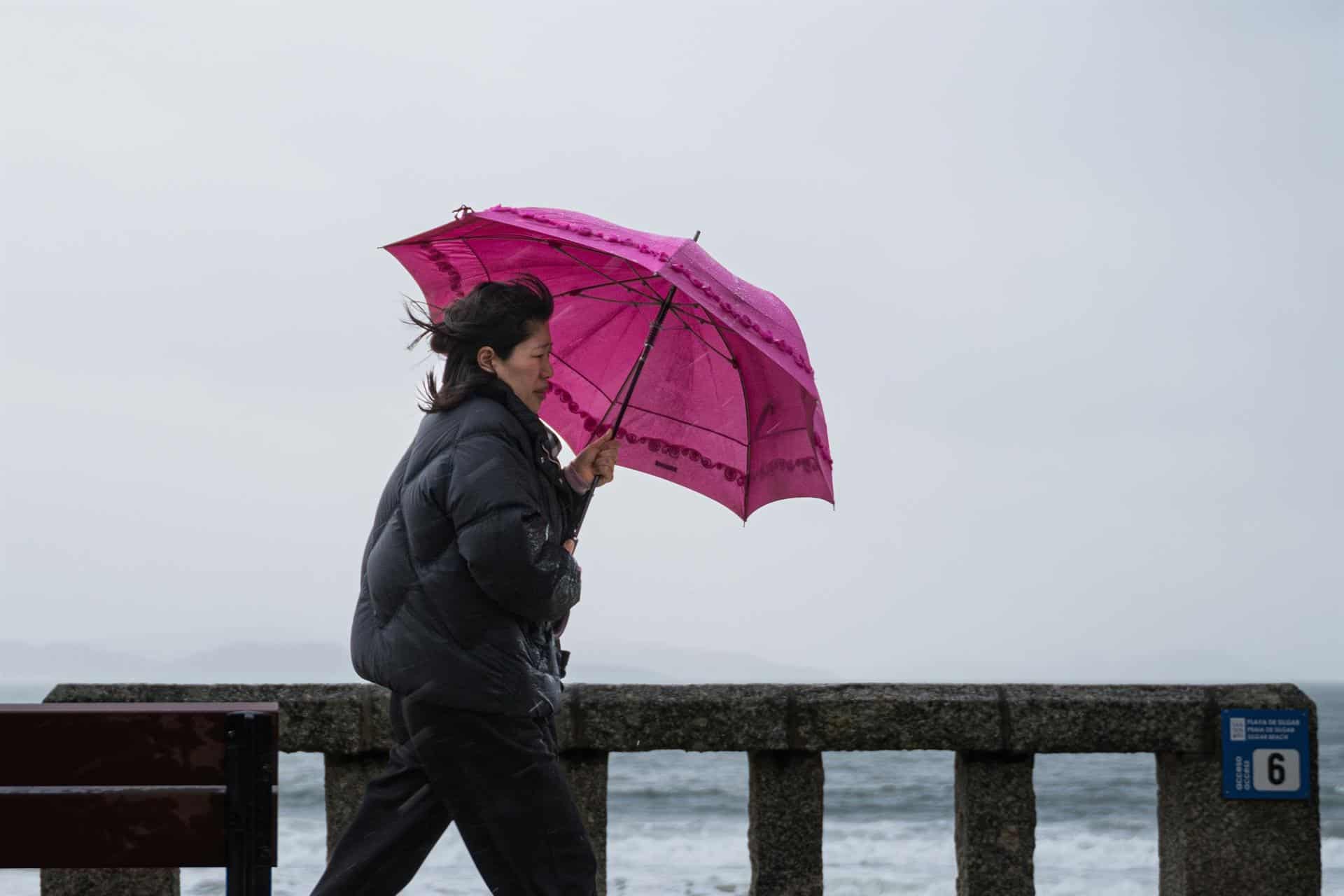 Una mujer se refugia de la lluvia con paraguas en el litoral gallego | EUROPA PRESS